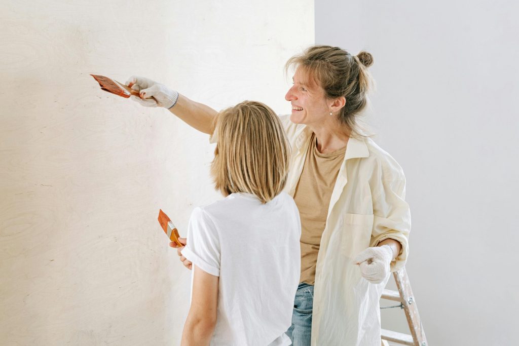 A smiling mother and child collaborate on painting a wall, showcasing a family home project.